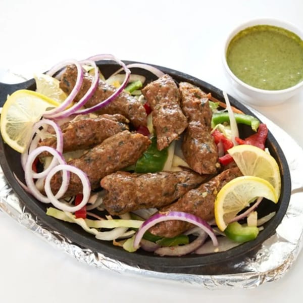 Abhiruchi Grill's Indian seekh kebabs with lemon, onions, and green chutney on a sizzling platter.