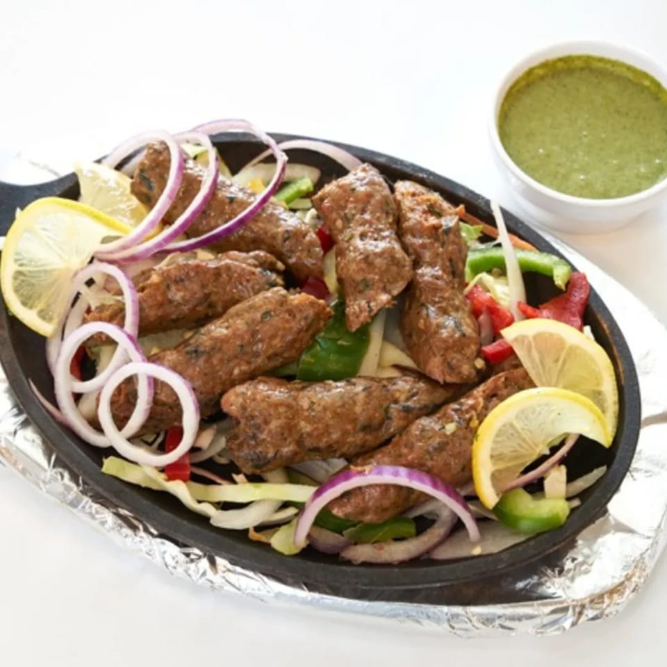 Abhiruchi Grill's Indian seekh kebabs with lemon, onions, and green chutney on a sizzling platter.
