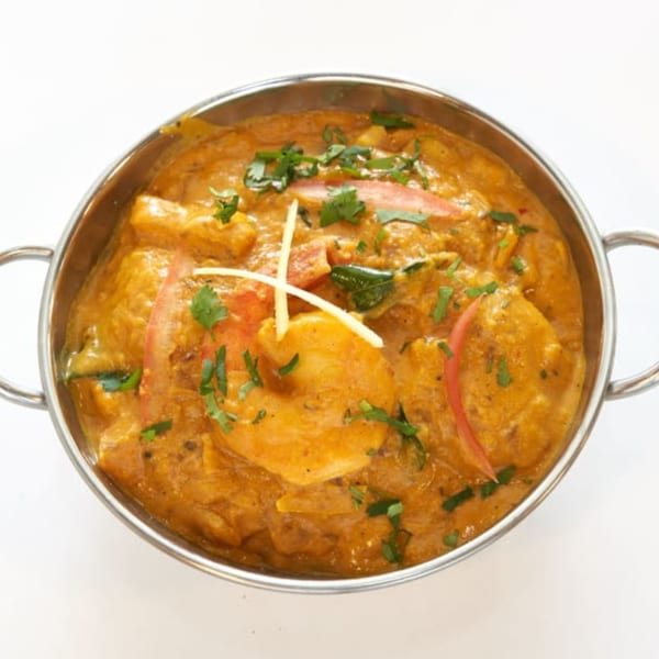Abhiruchi Grill's Indian curry, garnished with cilantro and ginger, served in a steel bowl.