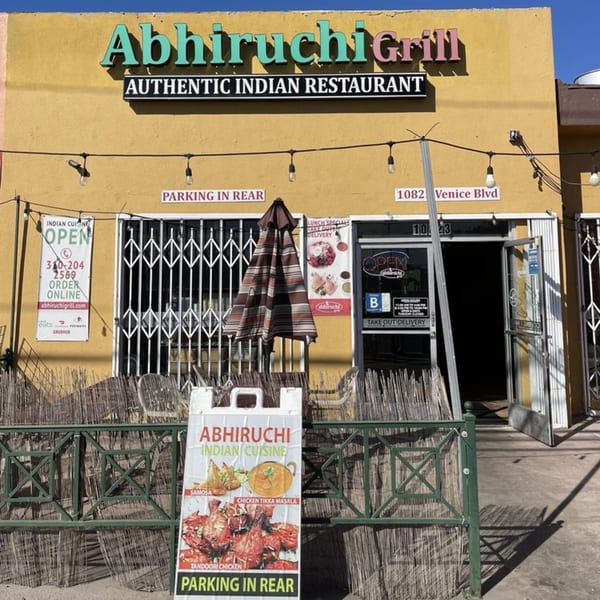 Exterior of Abhiruchi Grill, an Indian restaurant, with a yellow facade, signs, and an open door.