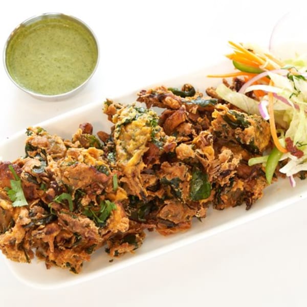 Crispy fried Indian pakora with green chutney and a side salad on a white plate.