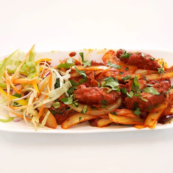 Abhiruchi Grill's chili chicken, a vibrant red dish with onions, cilantro, and a side salad.