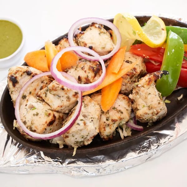 Abhiruchi Grill's chicken tikka, garnished with onions, carrots, bell peppers, and lemon, with a side of green chutney.