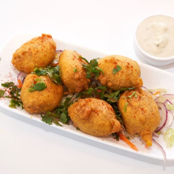 Six golden-fried Indian pakoras, garnished with cilantro and spices, served with a side of dipping sauce.