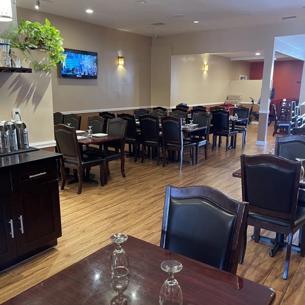 Interior of Abhiruchi Grill, an Indian restaurant, with empty tables and chairs, a TV, and plants.