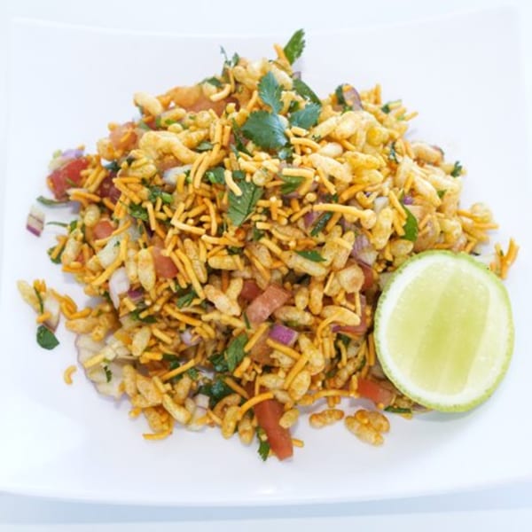 Bhel Puri, a popular Indian street food, with puffed rice, vegetables, and a lime wedge.